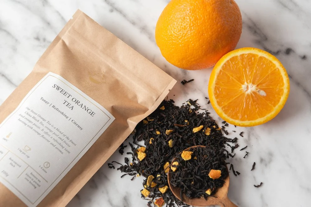 Orange Pekoe branded tea pouch with loose leaves and an orange on marble